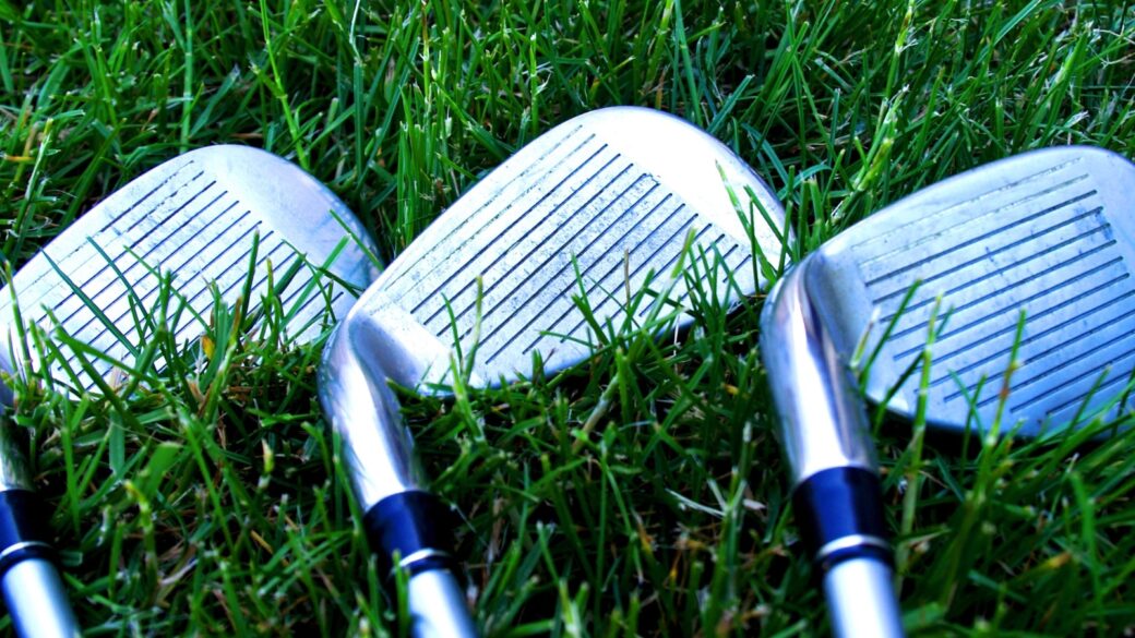 Three iron clubs lay on the rough of a golf course