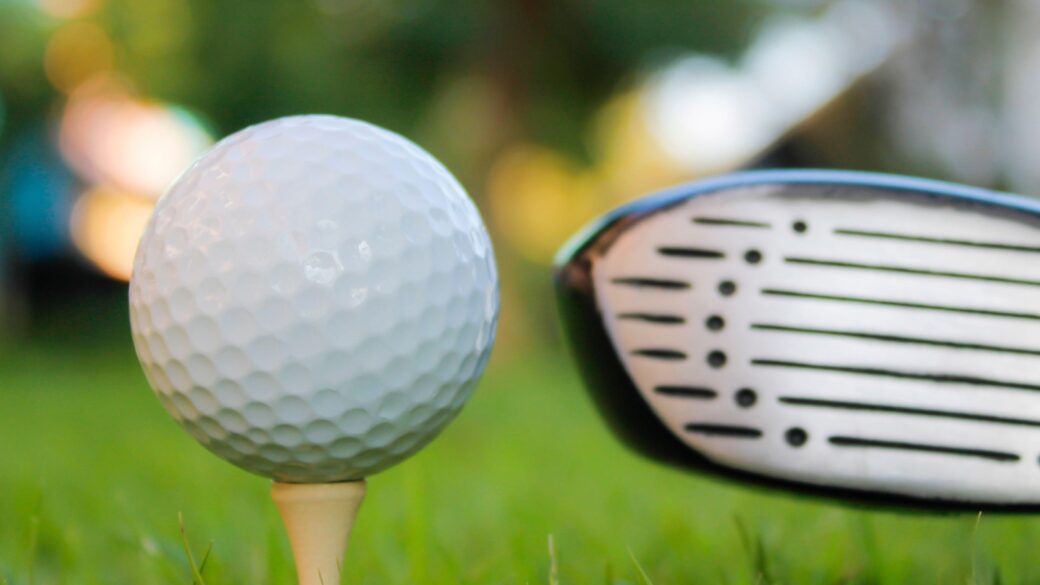 Golf ball set on tee in grass field, hit with one golf club, background with bokeh lights.